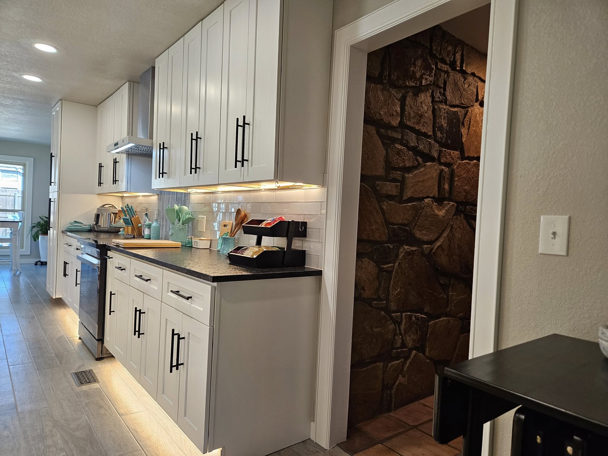A modern kitchen with white cabinets and a stone-walled entryway.