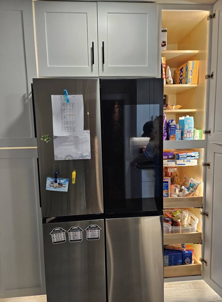 A person is in a kitchen, standing by a refrigerator and pantry.