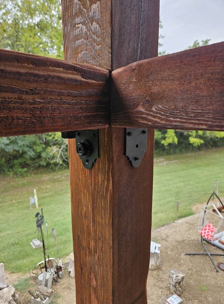 A security camera is mounted on a wooden post supporting a pergola outdoors.