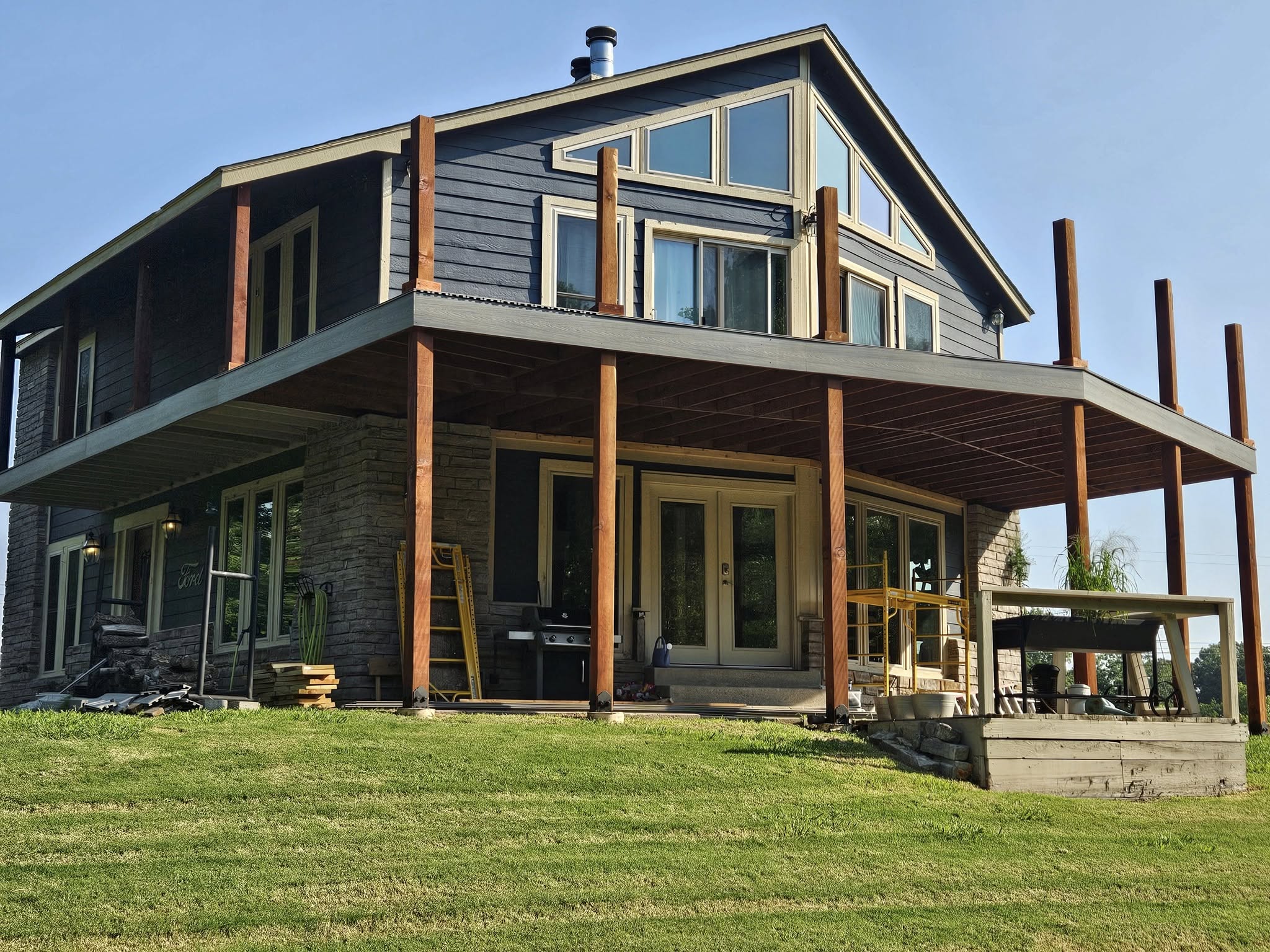 A modern house with a large deck is shown outdoors on a sunny day.