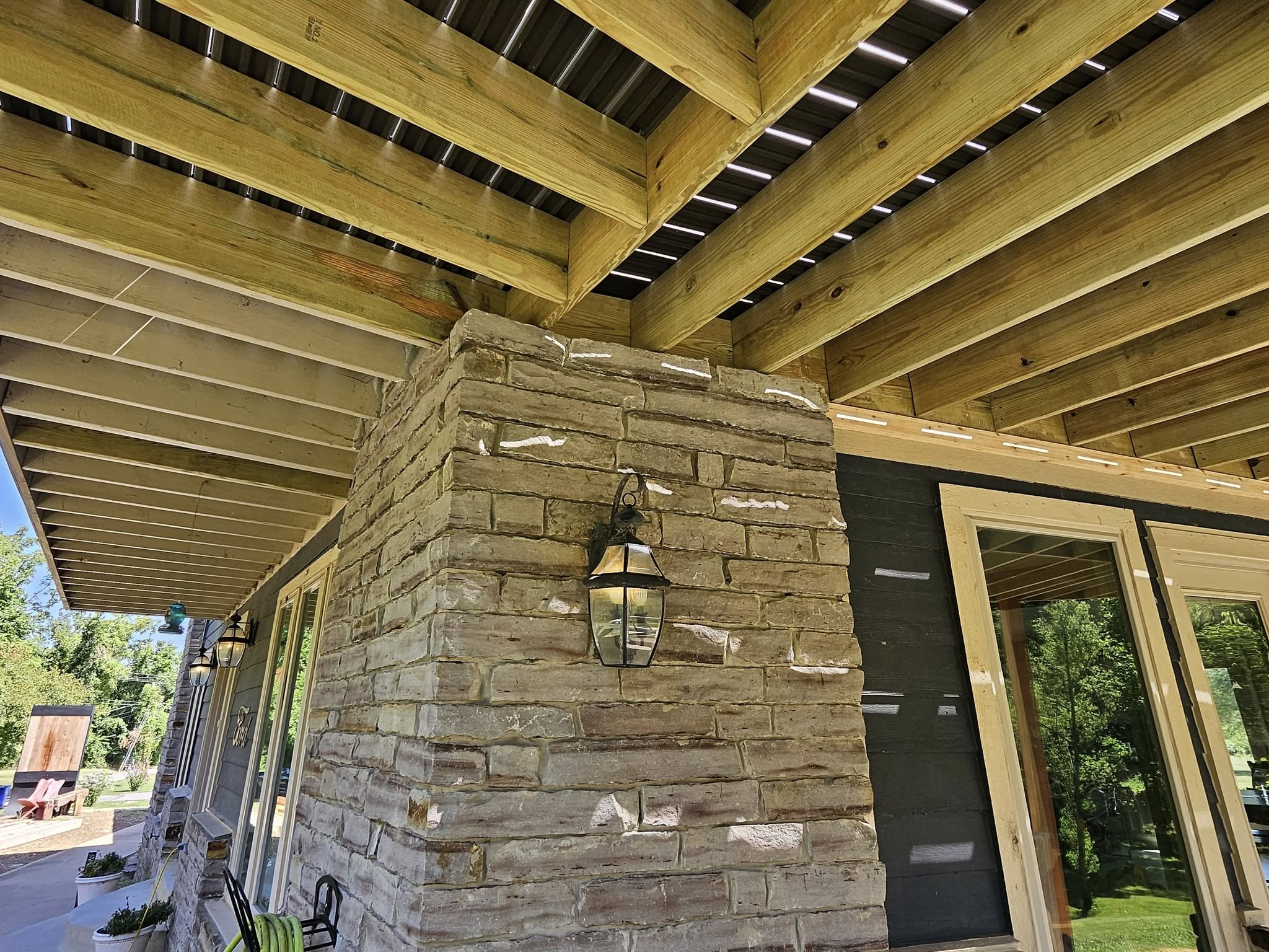 A stone-clad pillar supports a wooden deck structure on the exterior of a house.