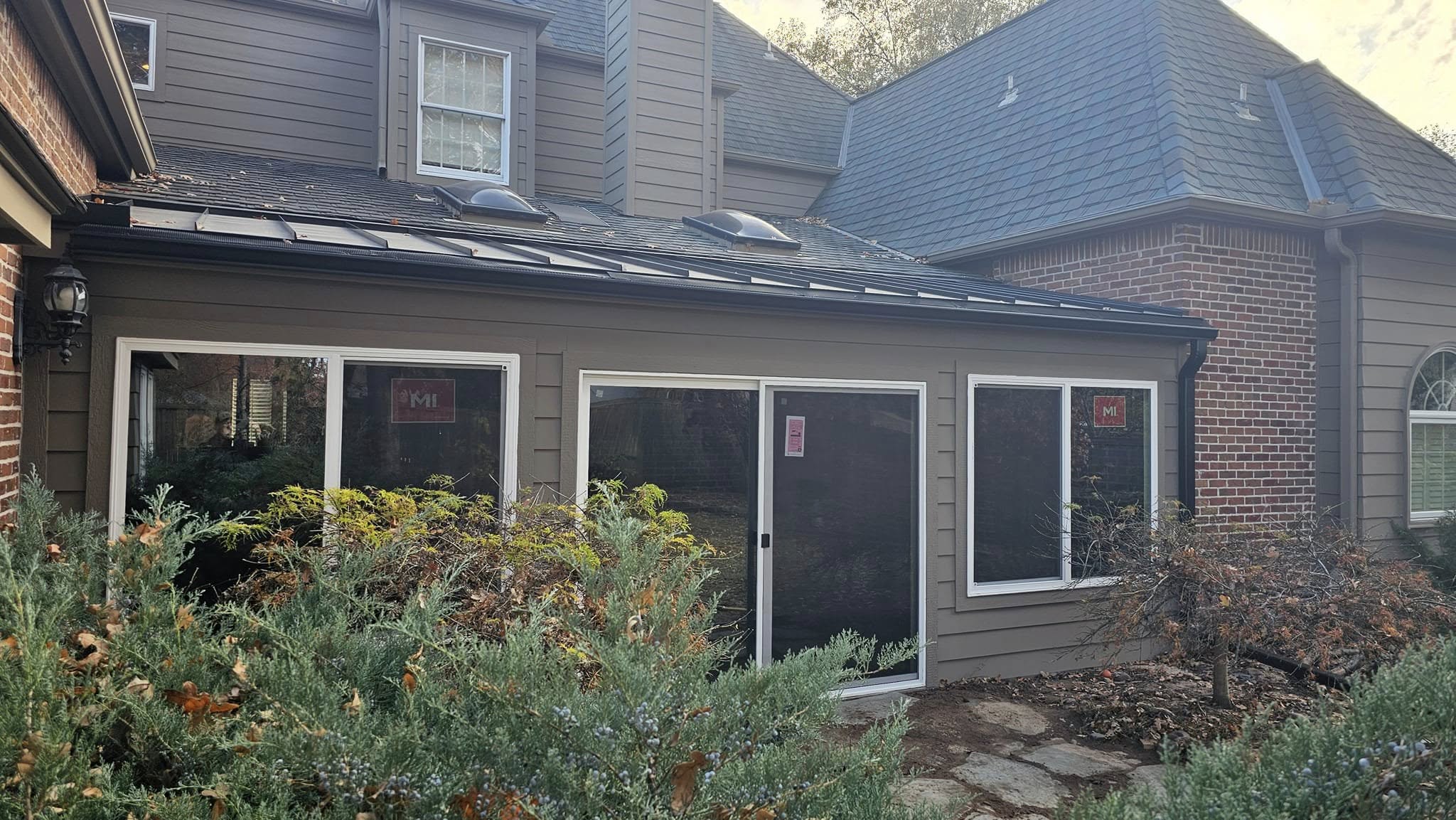A house with brown siding and a dark roof, featuring several windows and skylights.