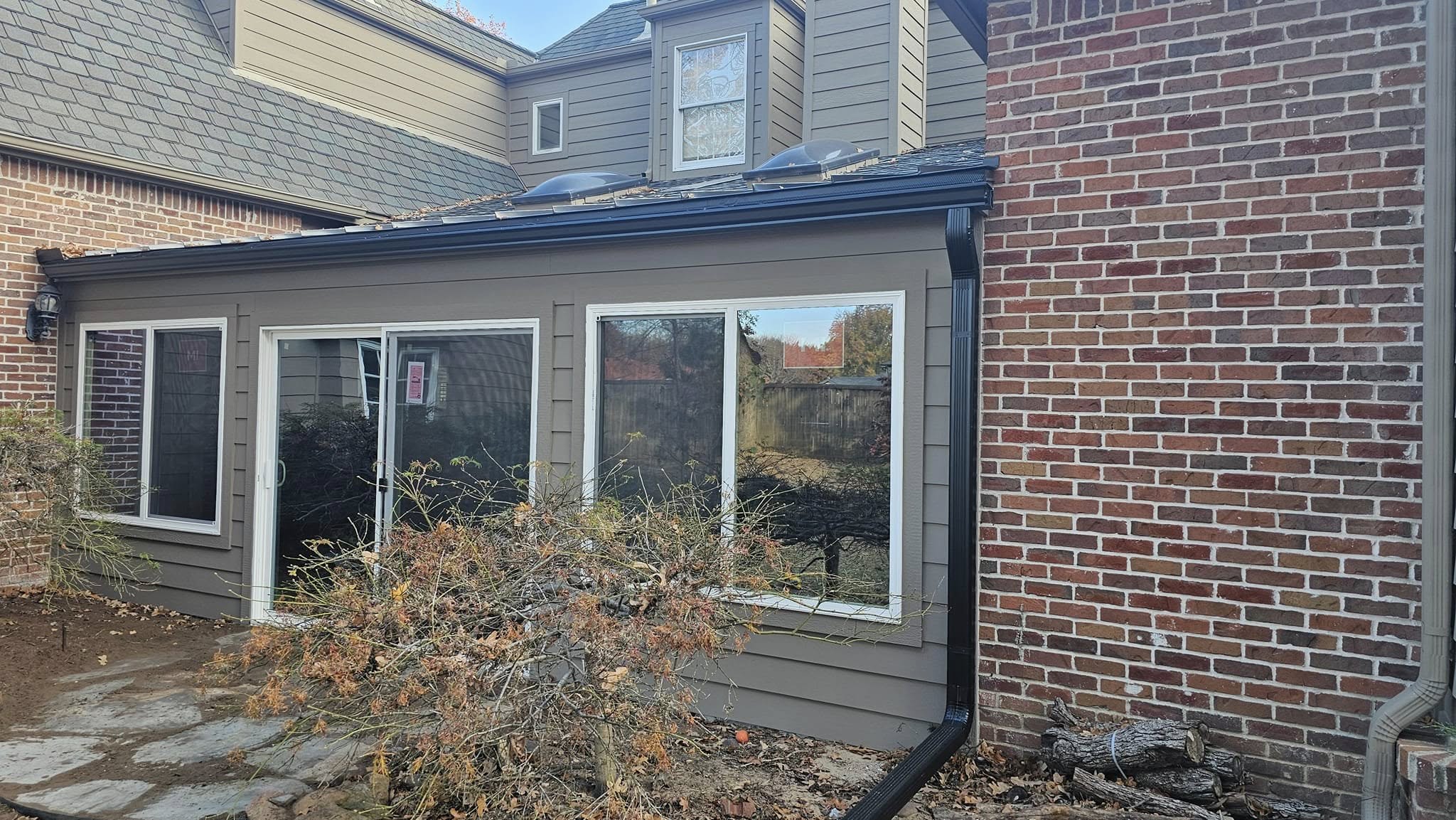 A house addition with large windows and a brick wall is shown outdoors.