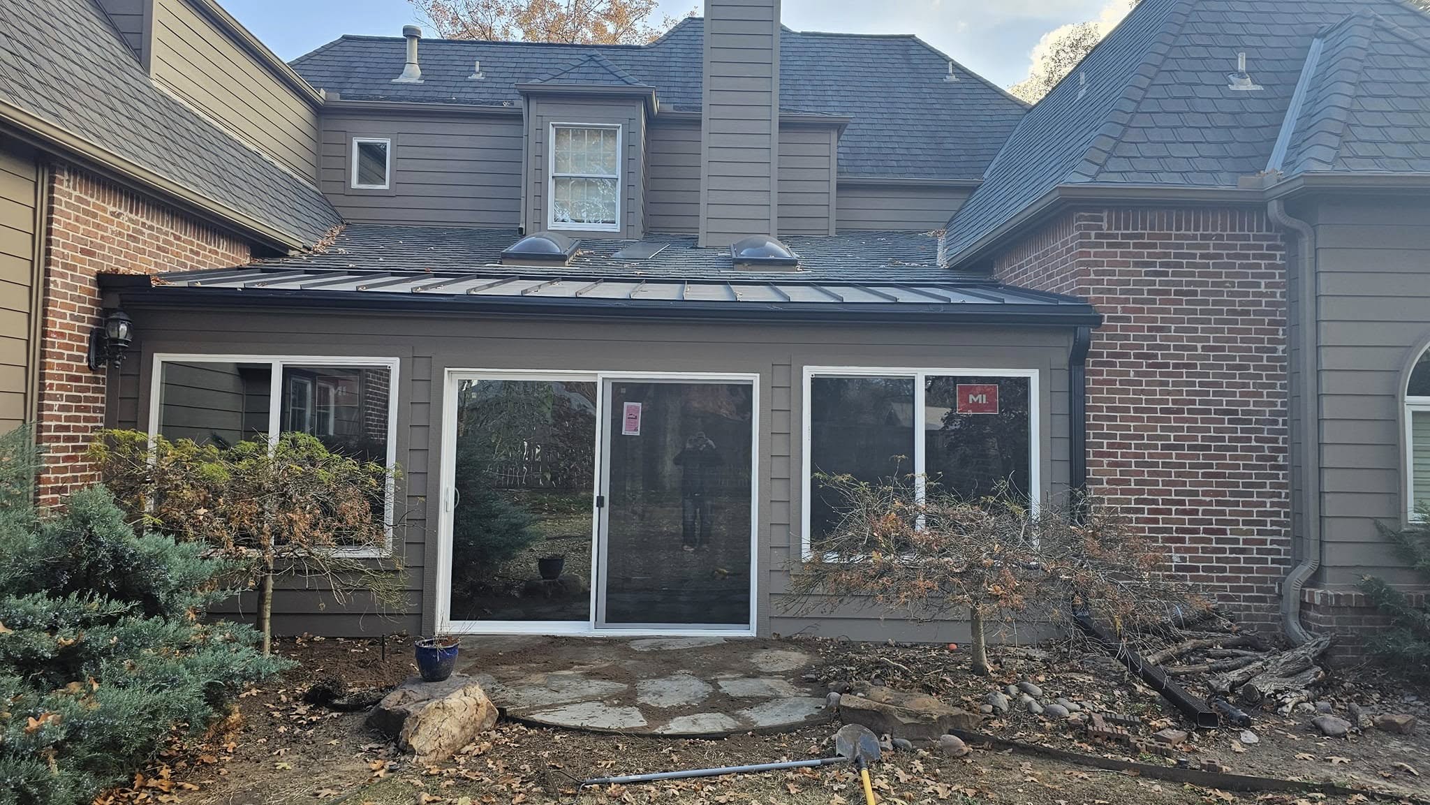 A house with a metal roof, sliding glass doors, and landscaping is shown outdoors.