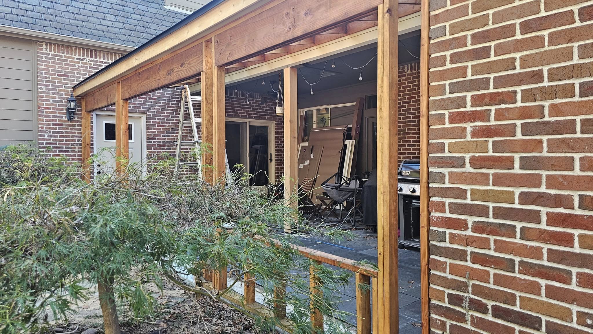 Construction of a wooden porch addition to a brick house with a grill and furniture.