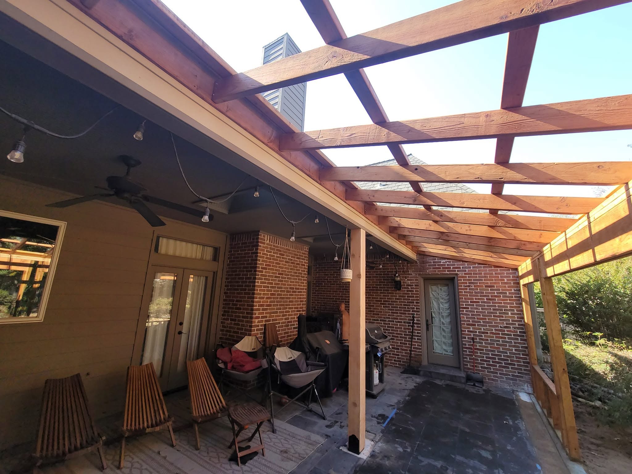 An outdoor patio with a wooden pergola, furniture, and a grill.