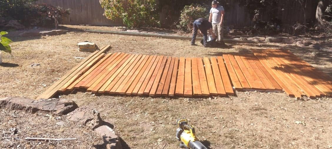 Two men are in a yard with lumber laid out on the ground.